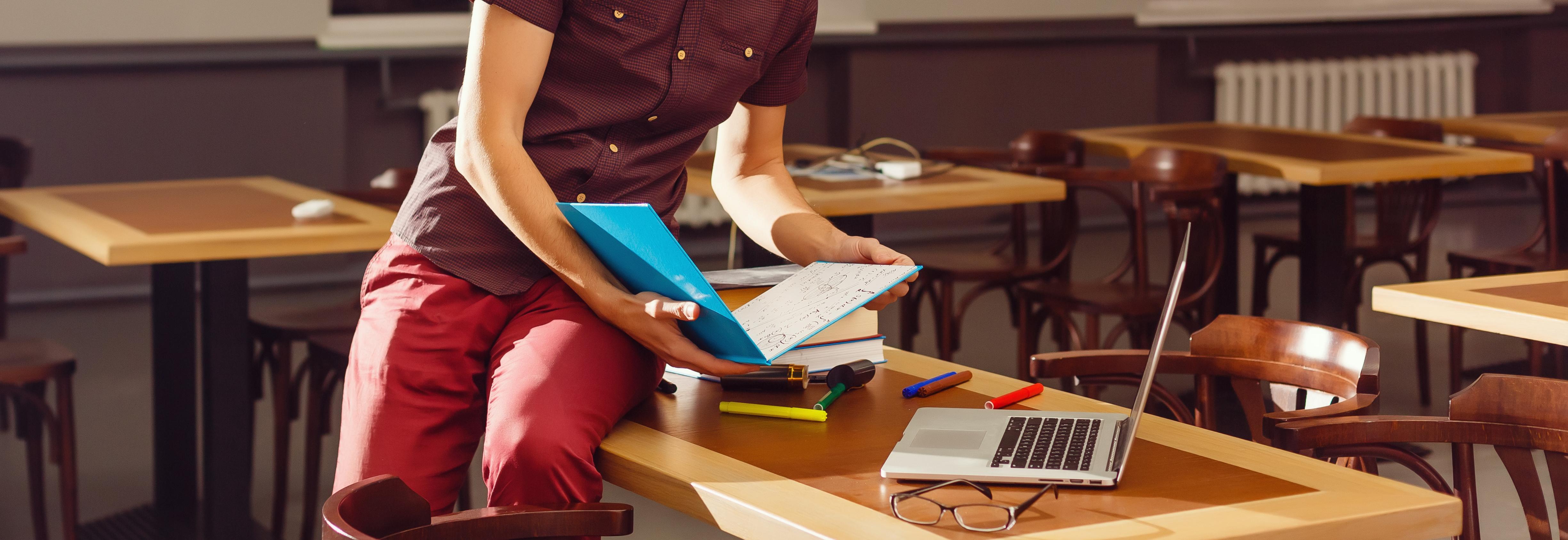 teacher with folder in hand while working on laptop